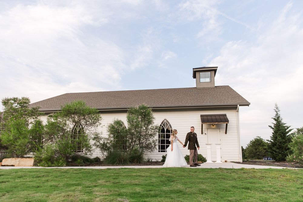 Newlyweds pose in front of a charming white chapel building with rustic architectural details.
