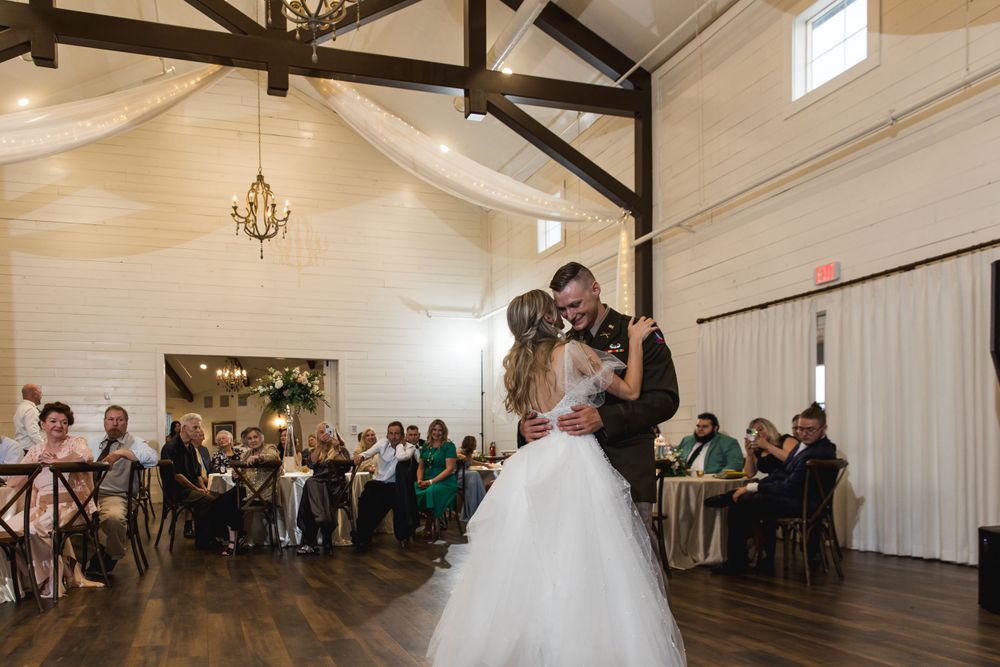 First dance in an elegant white reception venue with exposed wooden beams and draped fabric.