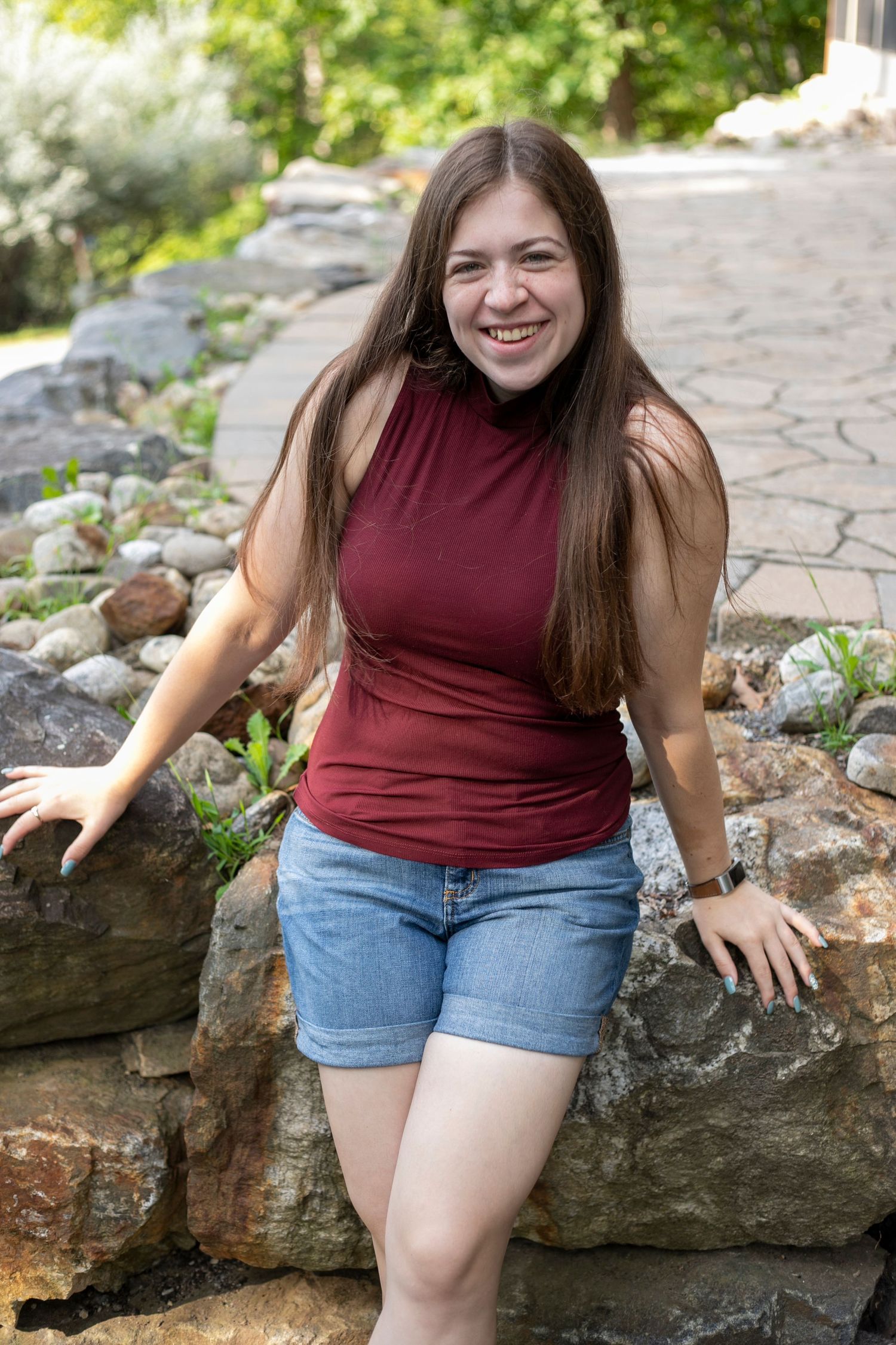 A Woman leaning on rocks wearing a burgundy shirt smiling