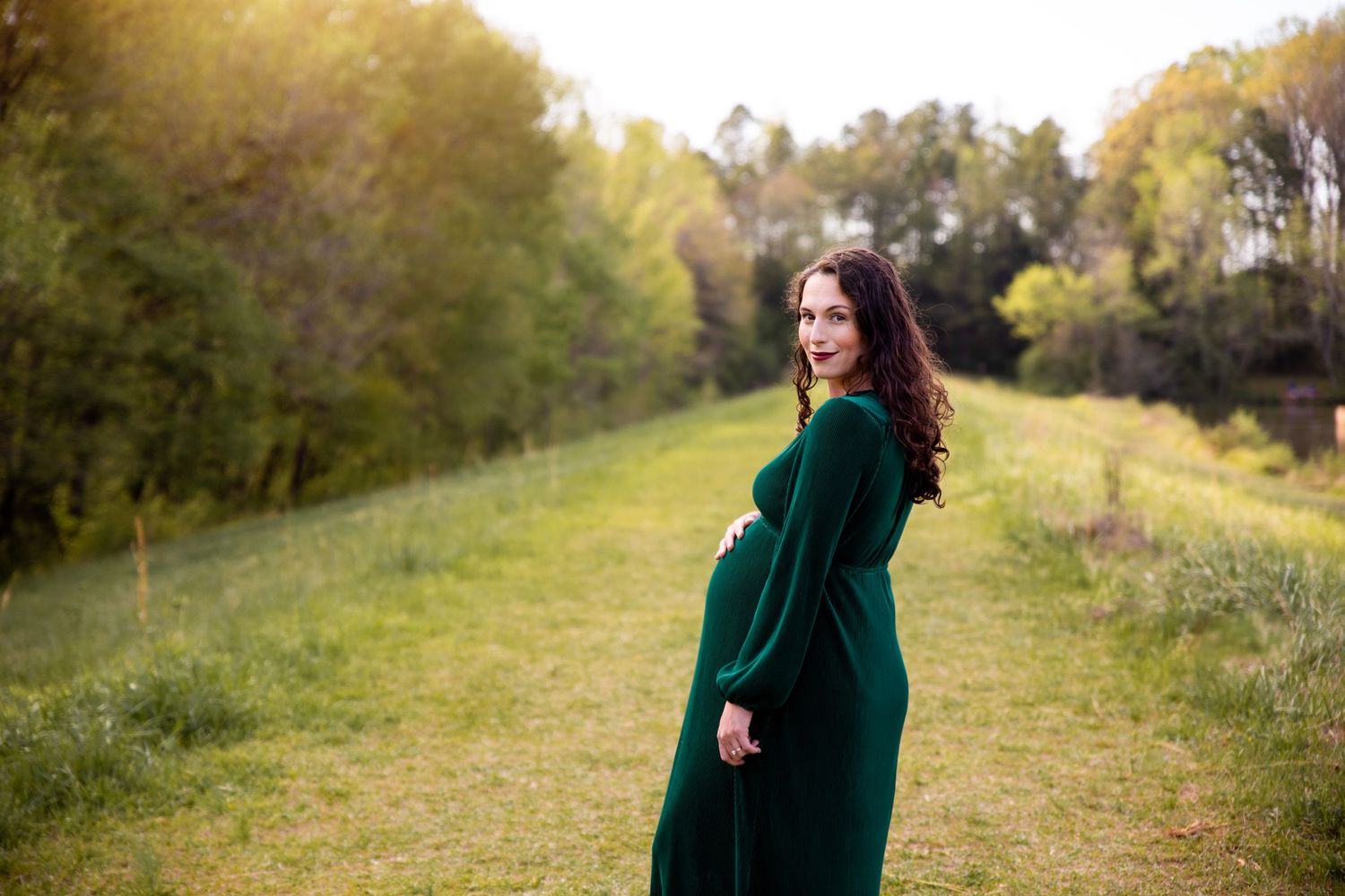 Maternity portrait on grassy hill with figure in emerald green dress.