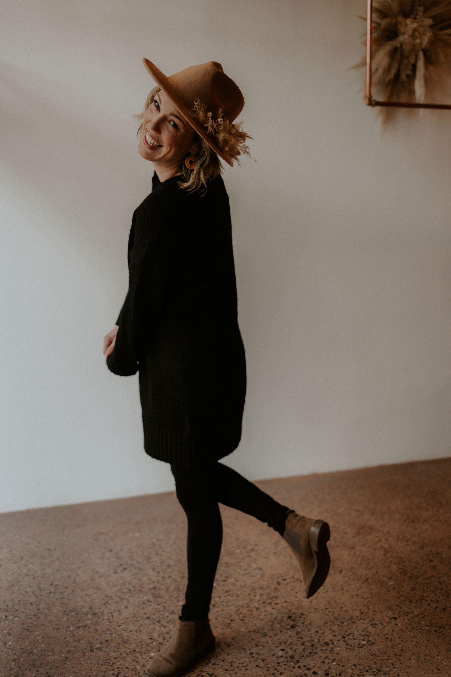 Candid portrait of someone in all black attire and brown hat walking playfully.
