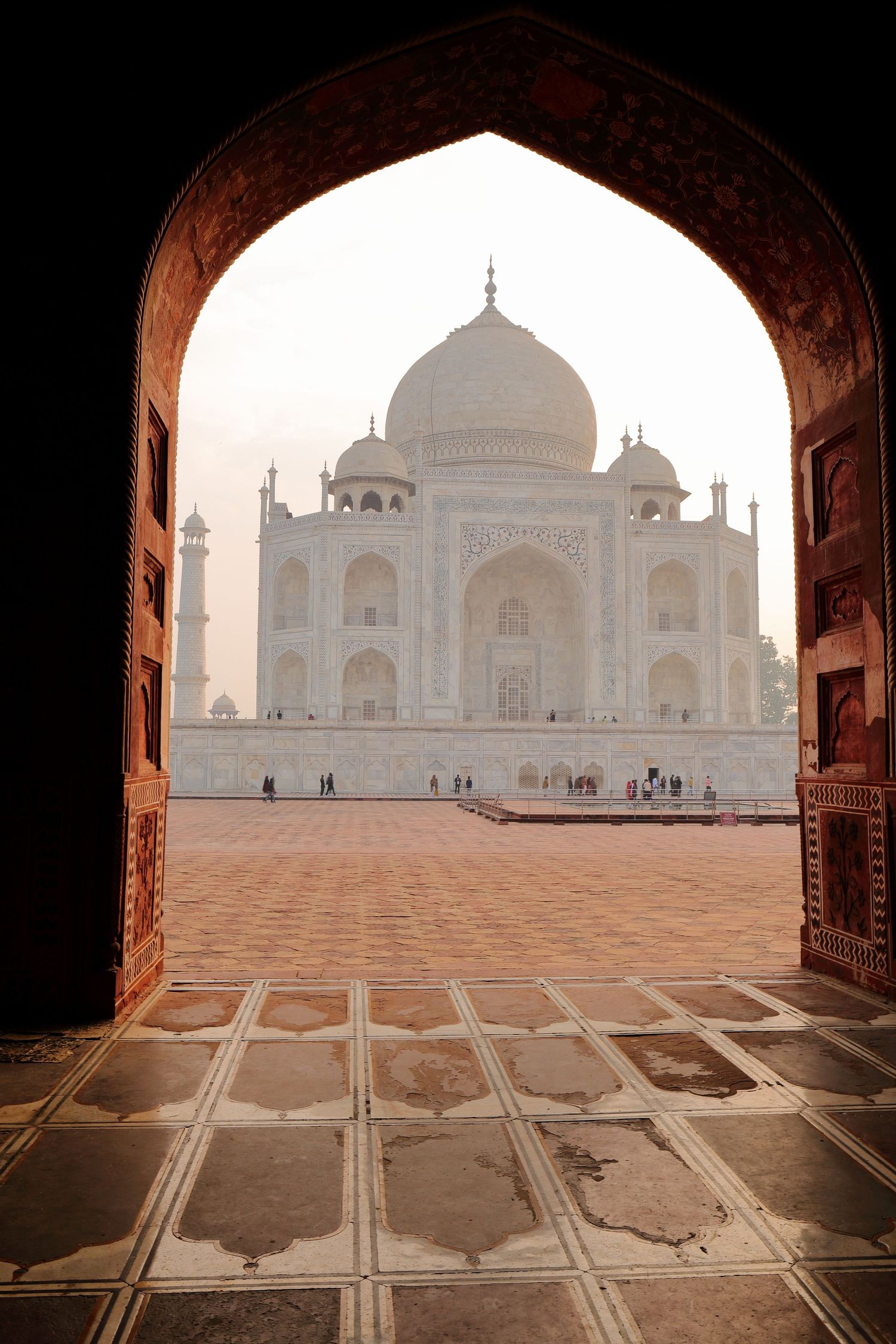 View of the Taj Mahal framed through an ornate archway at dawn.