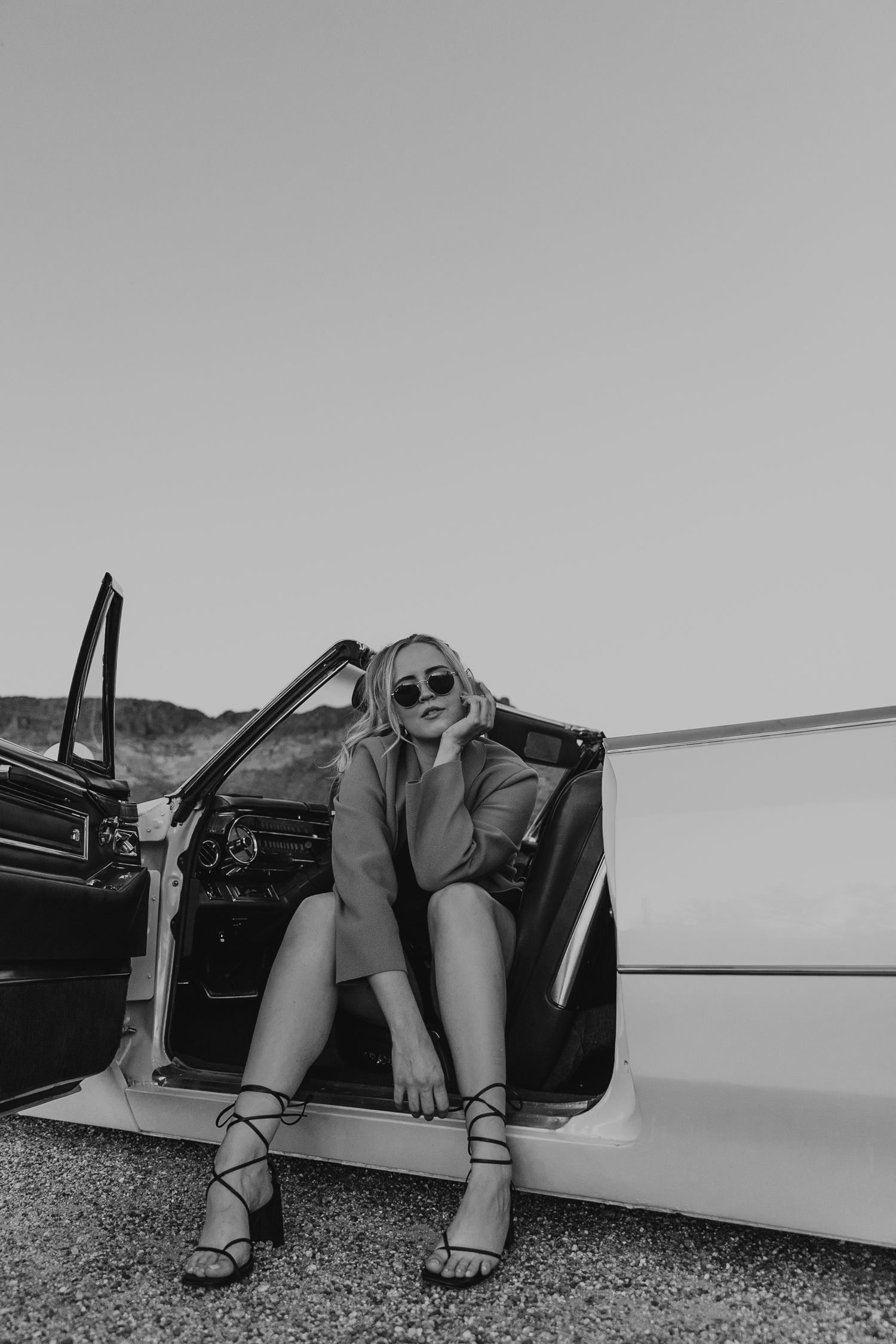 Vintage-style black and white portrait of woman sitting in classic car doorway. Arizona portrait photographer. Headshot photo AZ