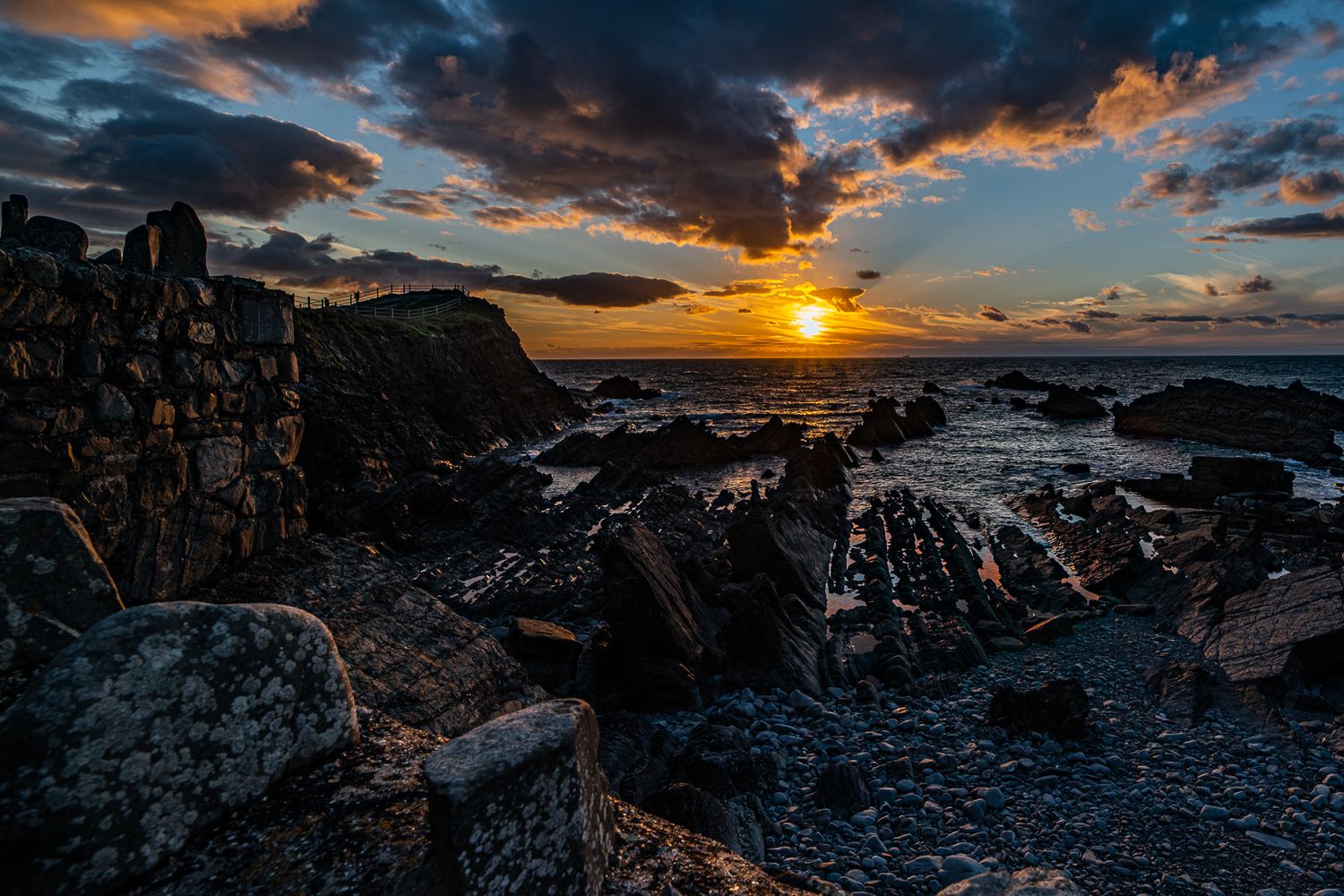 Dramatic sunset over rocky coastal cliffs with dramatic clouds and ocean waves.