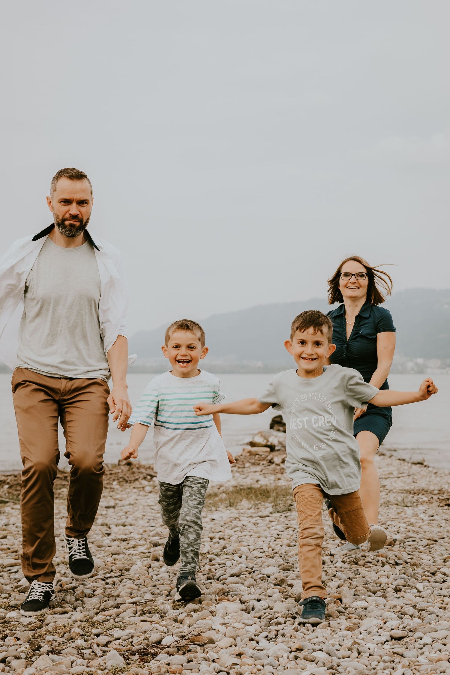 Happy family running and jumping on rocky beach shoreline.