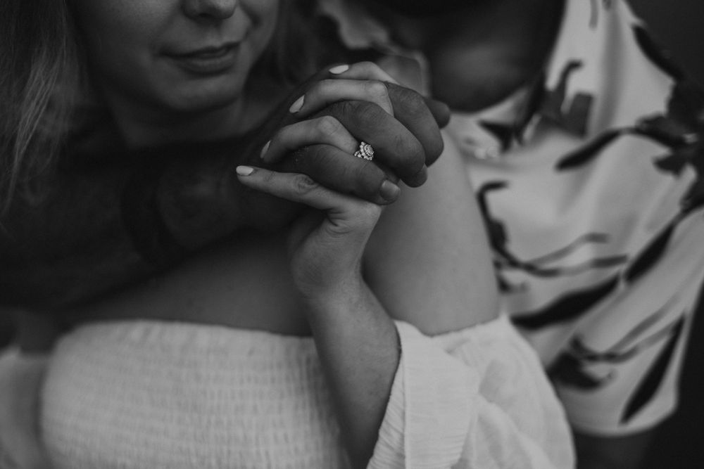 A close-up black and white shot showing hands clasped together with a soft focus white dress visible.