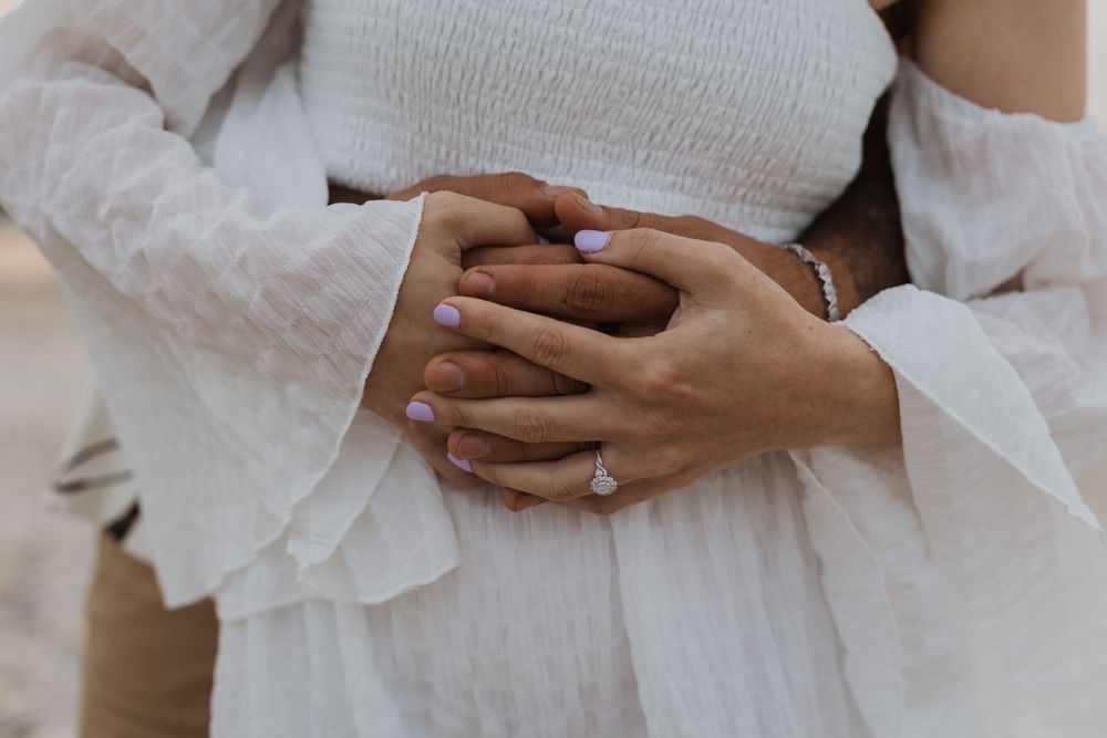 Intimate close up of hands clasped together with engagement ring visible.
