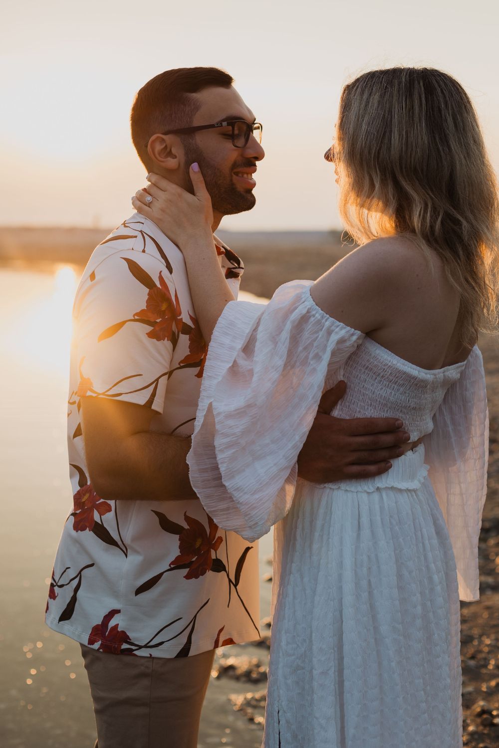 A romantic sunset embrace between two people wearing white and floral patterns.