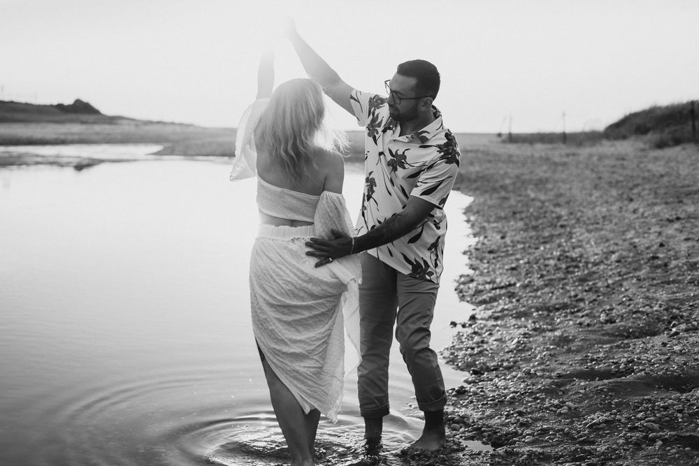 Couple dancing together at sunset by the water in black and white.