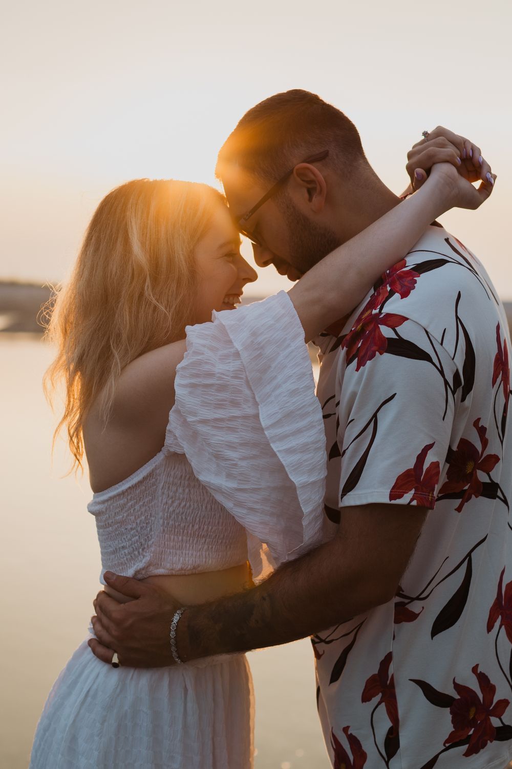 Intimate sunset portrait of couple dancing with golden light and floral shirt details.