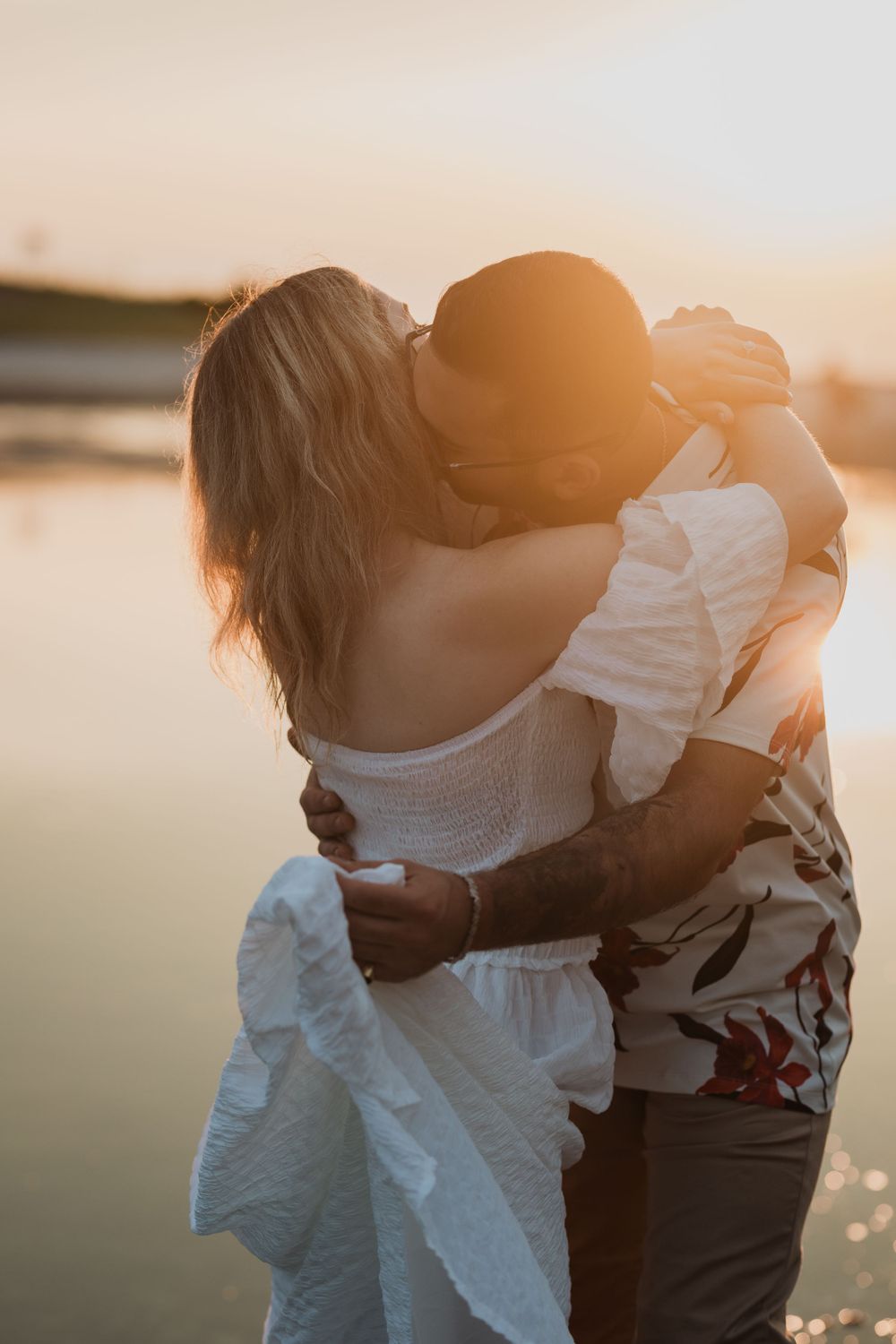 Couple embracing in warm sunset light by the water's edge.