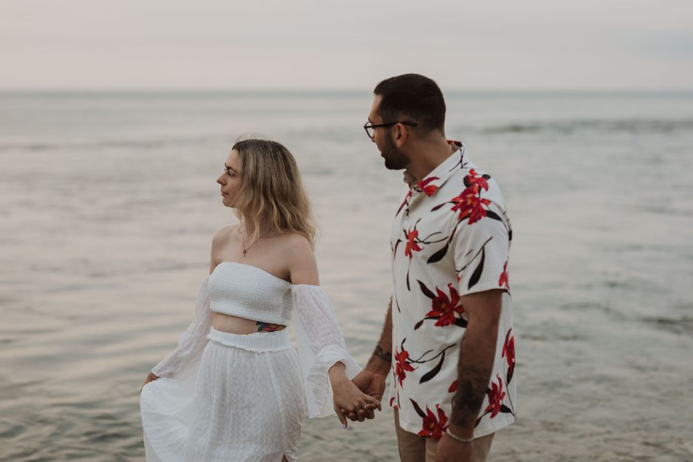 Couple holding hands while walking along shoreline at sunset.