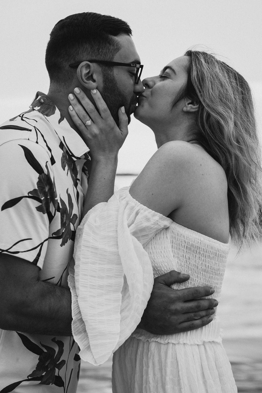 Romantic black and white photo of a couple sharing an intimate kiss on the beach.