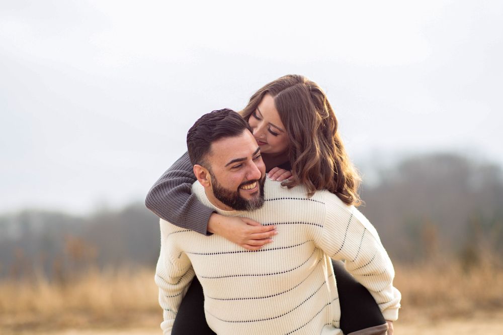 Playful autumn engagement photo showcasing a piggyback ride in matching sweaters.