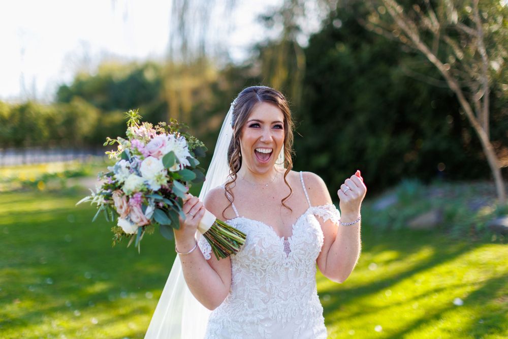 Excited bride holding bouquet of pink and white flowers in outdoor garden setting.