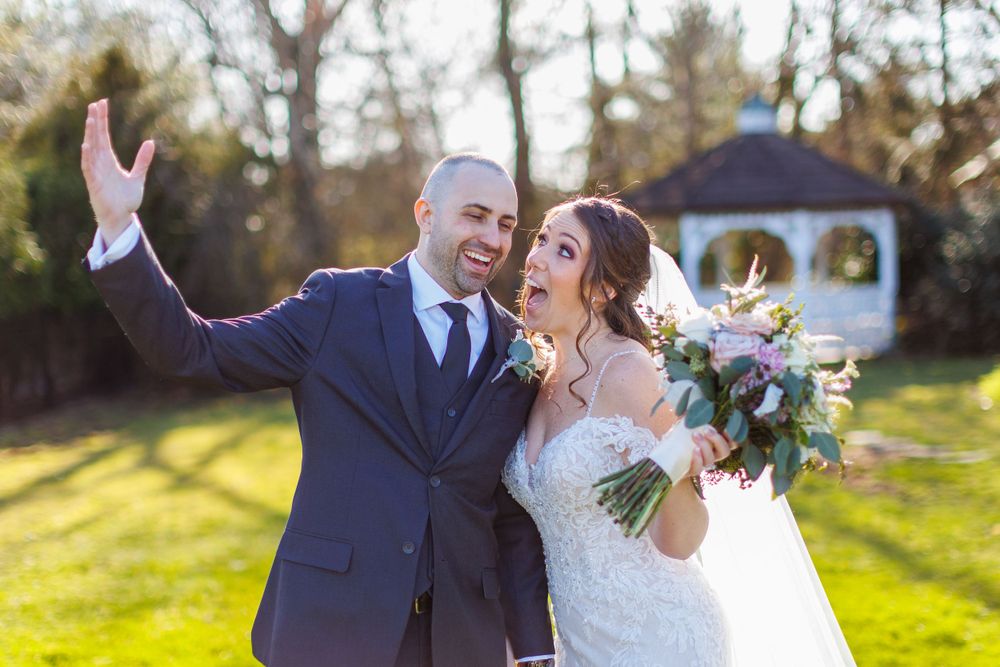 Joyful wedding couple celebrating in front of a garden gazebo during golden hour.