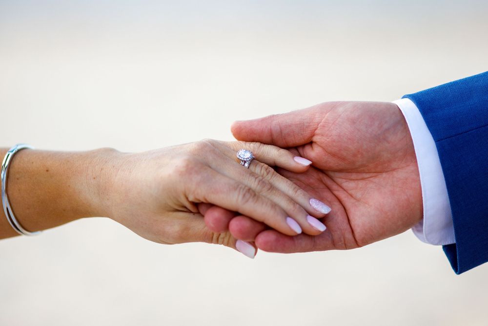 Close-up of bride and groom holding hands showing wedding rings.