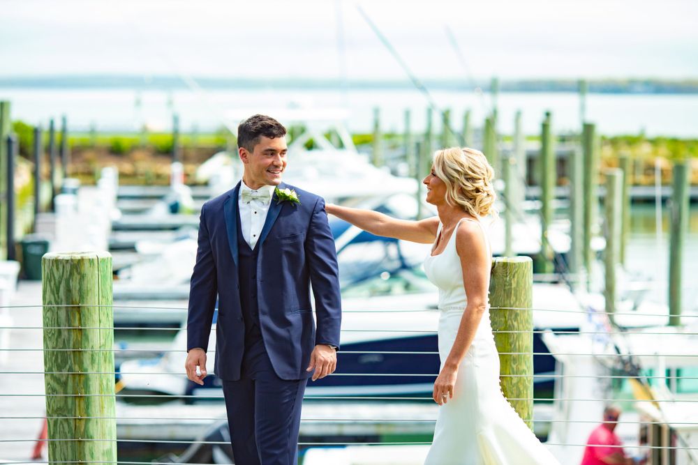 Elegant wedding couple posing on marina dock with boats in background.