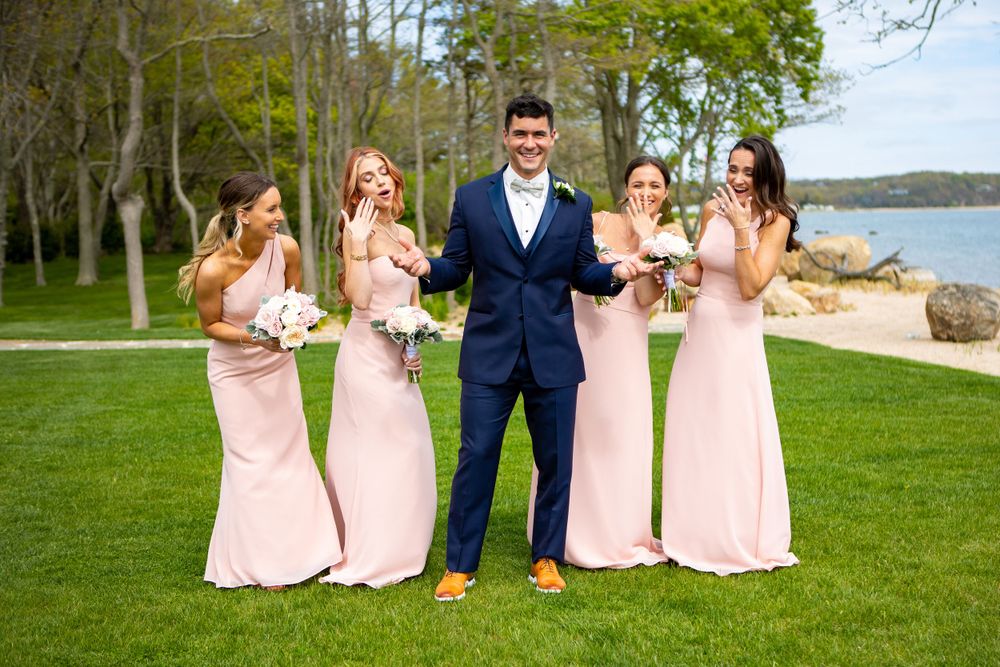 Wedding party poses on green lawn with bridesmaids in pink dresses and groom in navy suit.