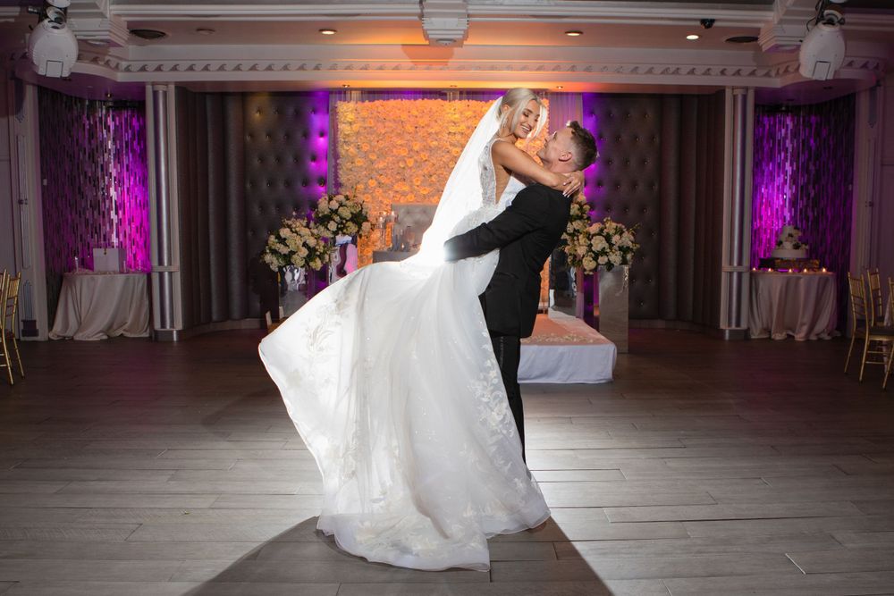 Couple performs romantic dance dip in elegant reception venue with purple uplighting.