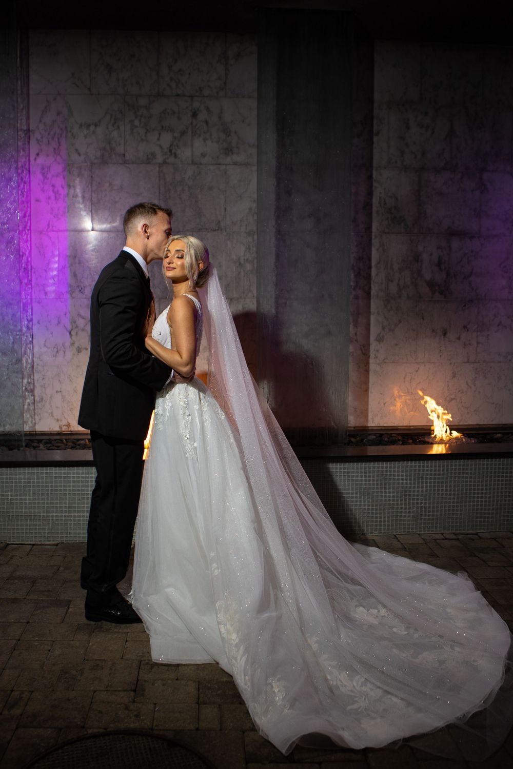 Couple shares intimate moment in dramatic lighting with flowing white wedding gown.