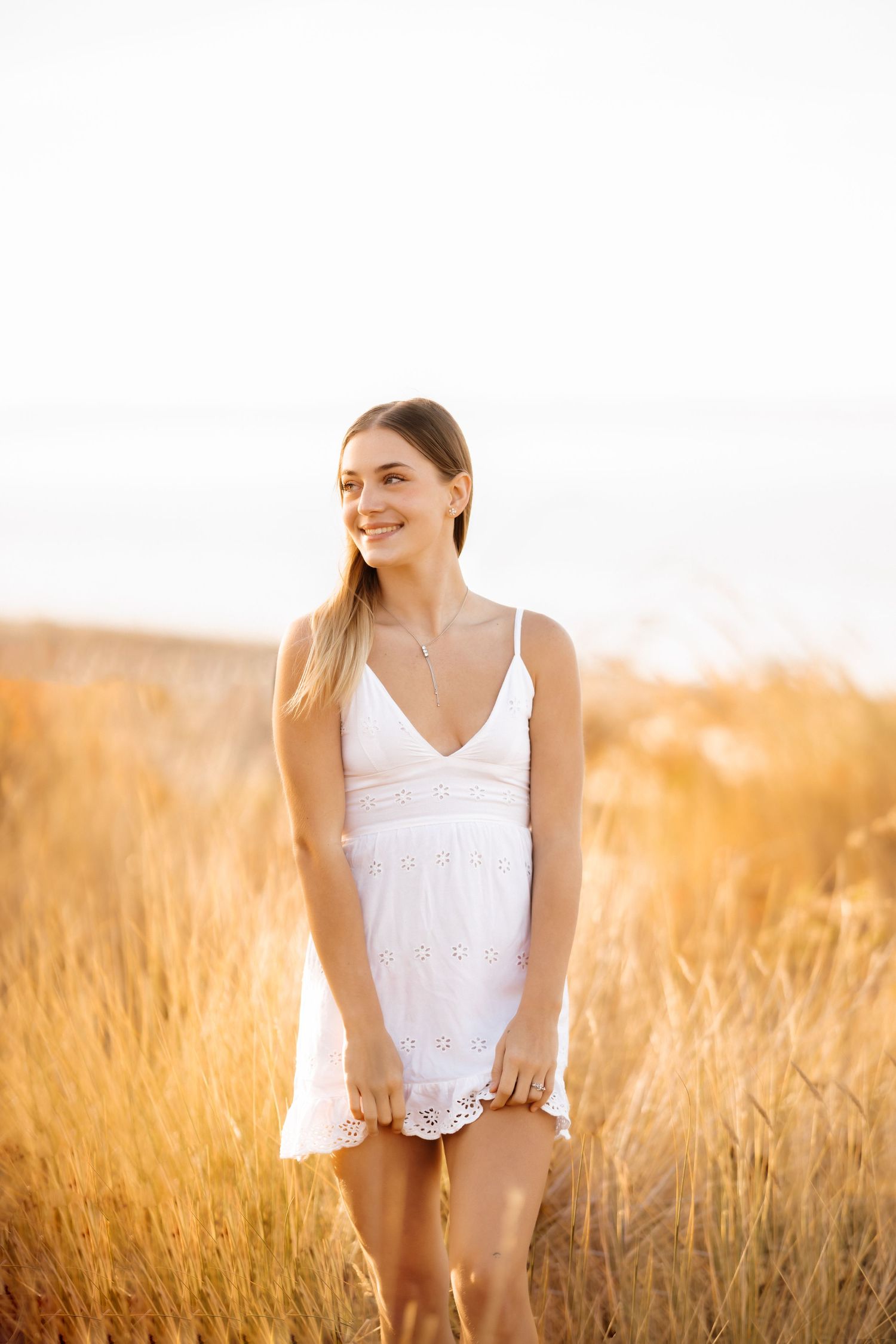 A woman in a white summer dress stands in a golden wheat field at sunset.