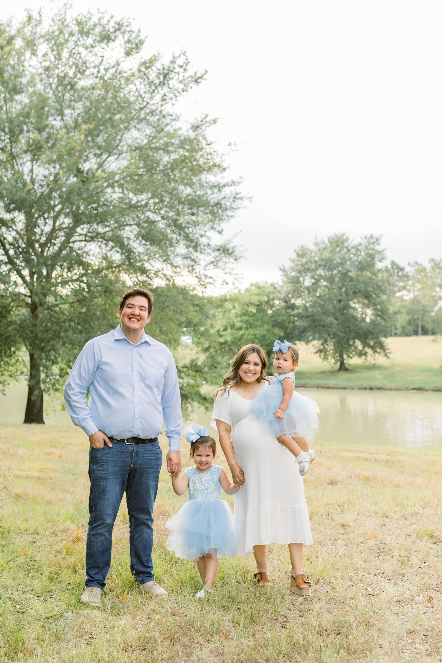 A family in coordinated blue and white outfits stands together in a scenic outdoor setting near a pond.