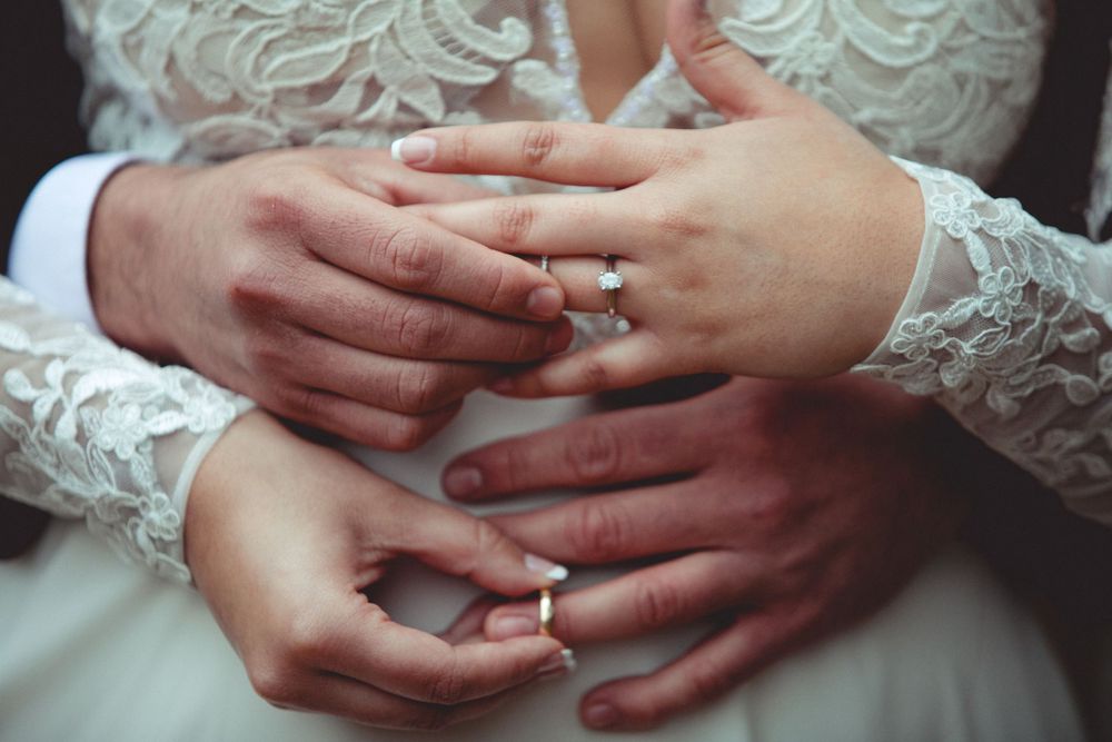 Close-up detail of hands with wedding rings and lace sleeves.