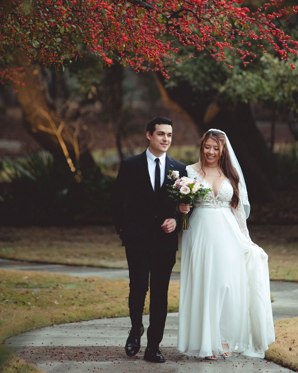 Wedding couple walking under beautiful red flowering trees in an autumn garden.