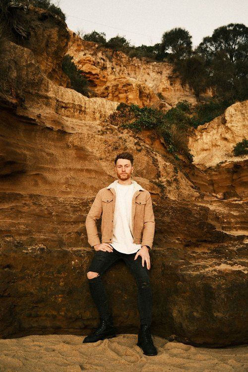 Person in tan jacket poses against dramatic rocky cliff face at sunset.