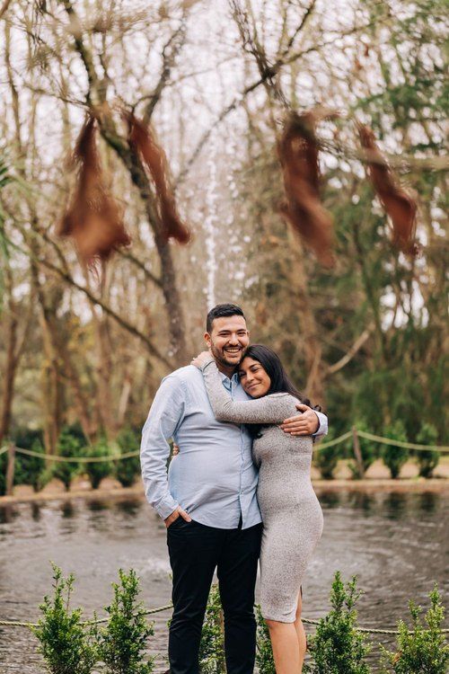 Couple embracing by pond in park wearing casual outfits.
