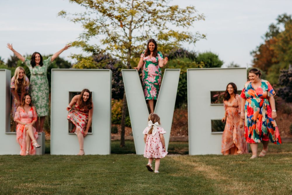 Group poses with large LOVE letters outdoors wearing colorful floral dresses.