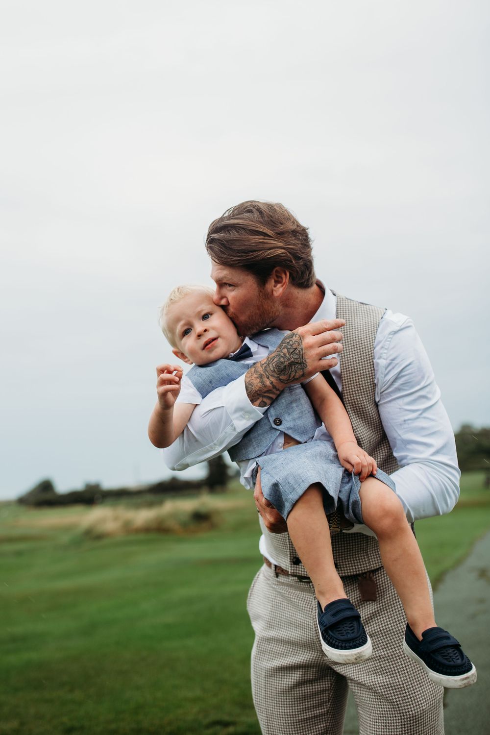 Parent shares tender moment with small child on grassy hill.