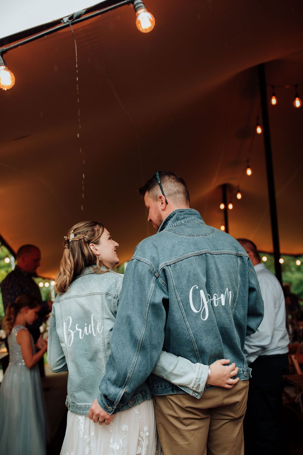 Matching customized denim jackets with 'Bride' and 'Groom' text under warm reception lighting.