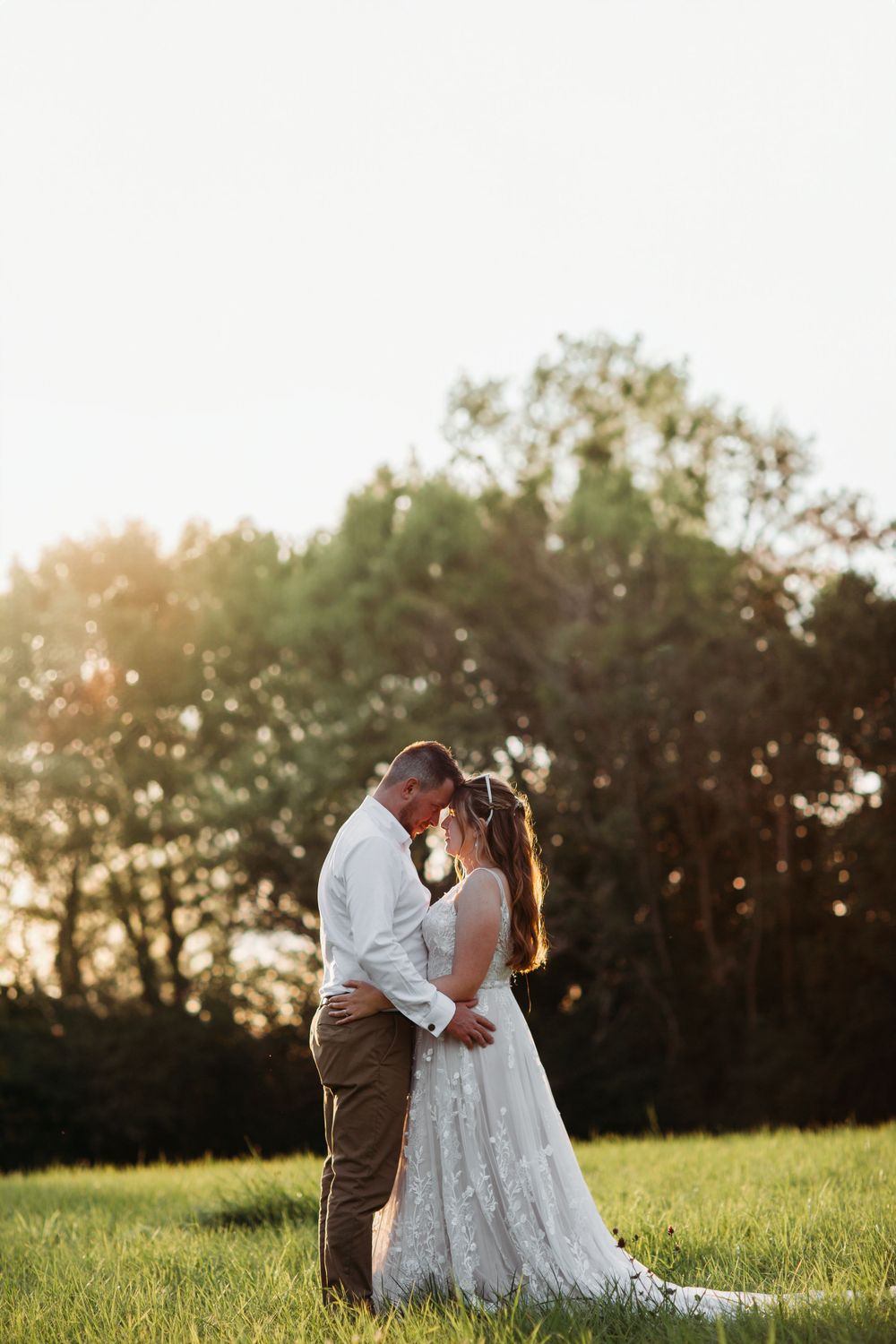 A backlit couple embraces in a sunlit field during golden hour.