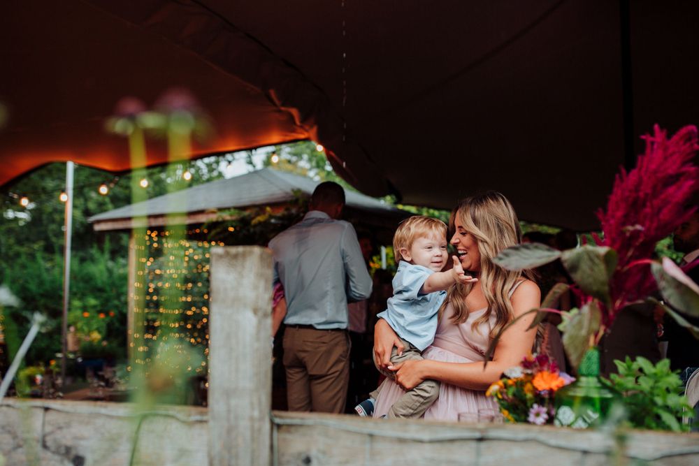 A festive outdoor wedding reception under a tent with string lights and colorful floral arrangements.