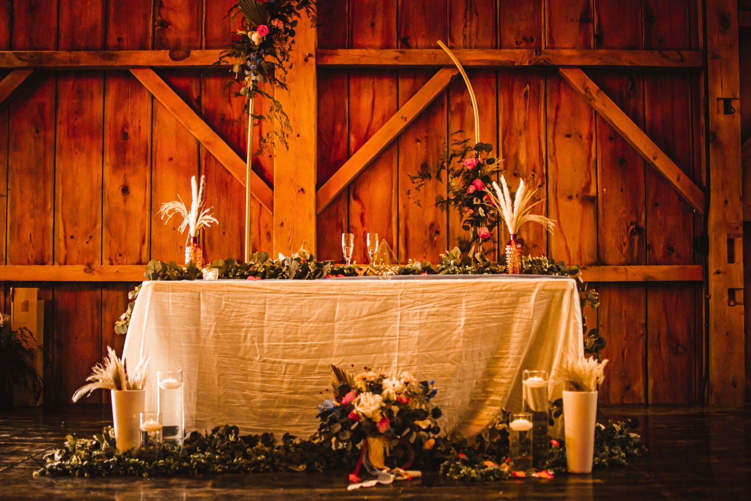 Rustic barn wedding reception table with white linens, candles and floral decorations.