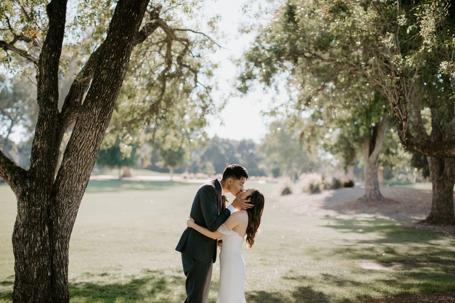 A romantic moment shared between newlyweds under the shade of oak trees.