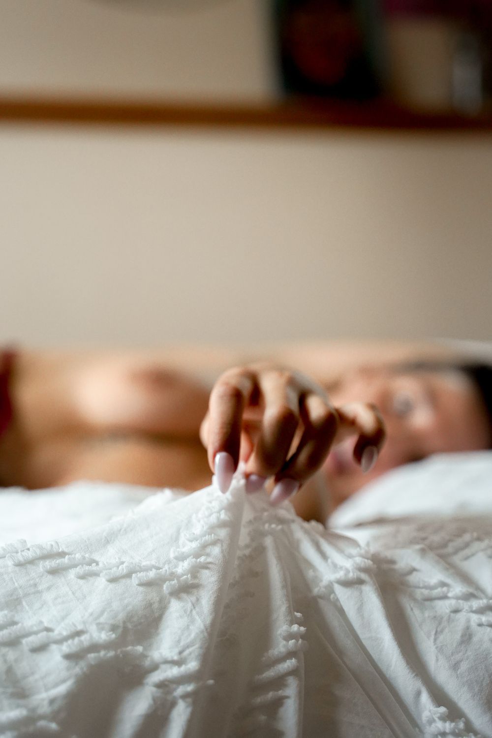 Close-up of hand gripping white bedsheets in soft natural light.
