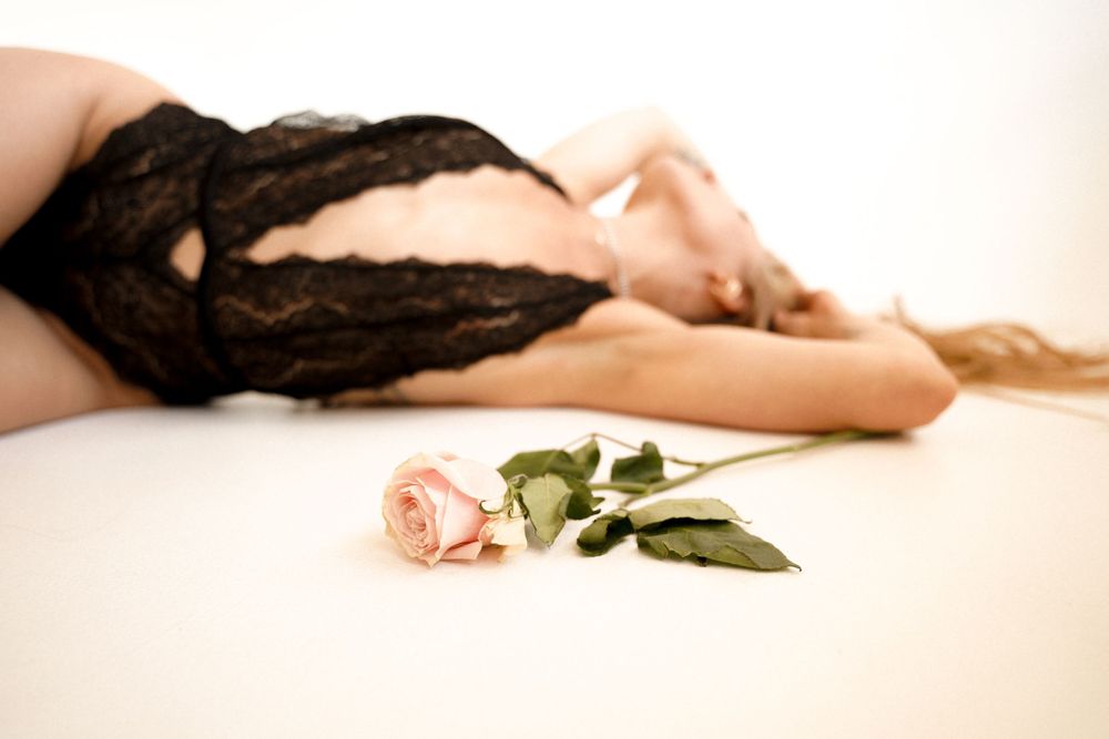 A pink rose lies on a white surface beside a person wearing black lace lingerie.