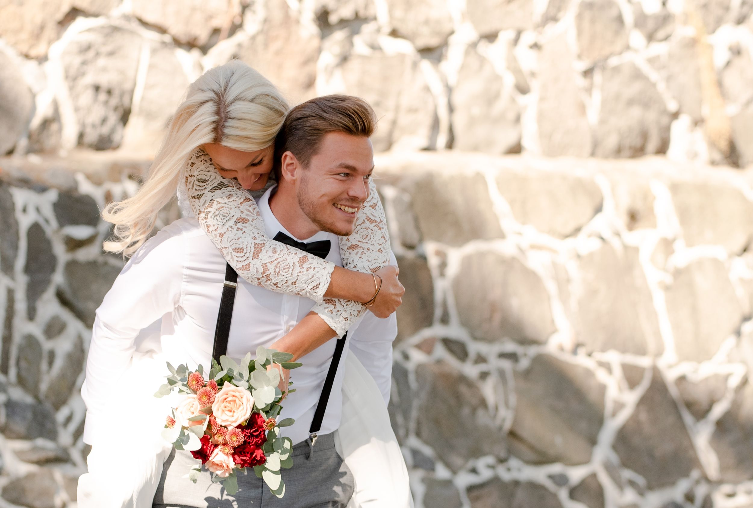A joyful wedding moment captured against a stone wall background with bright sunlight.