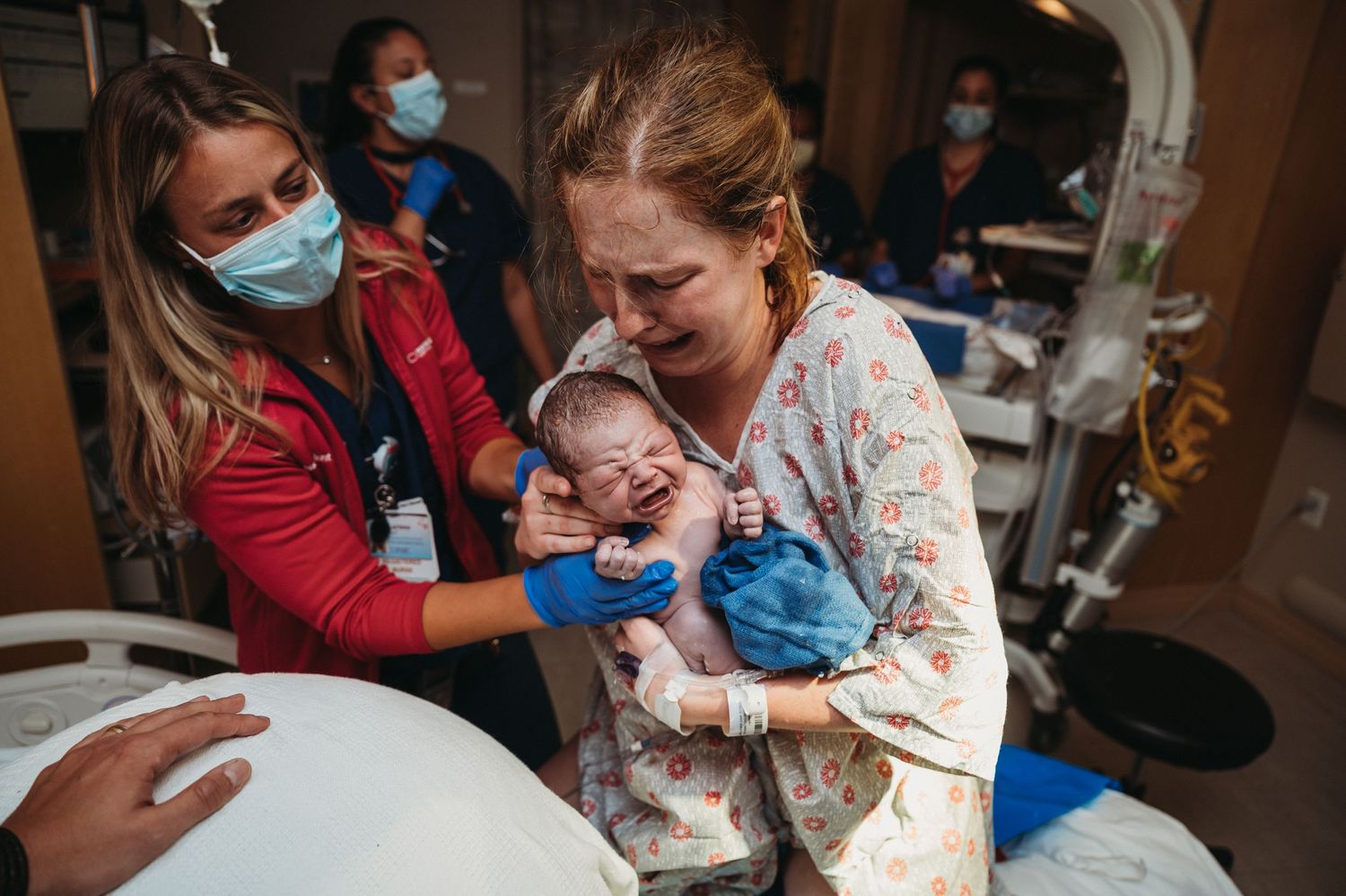 Emotional mother crying while holding newborn baby in hospital after delivery.