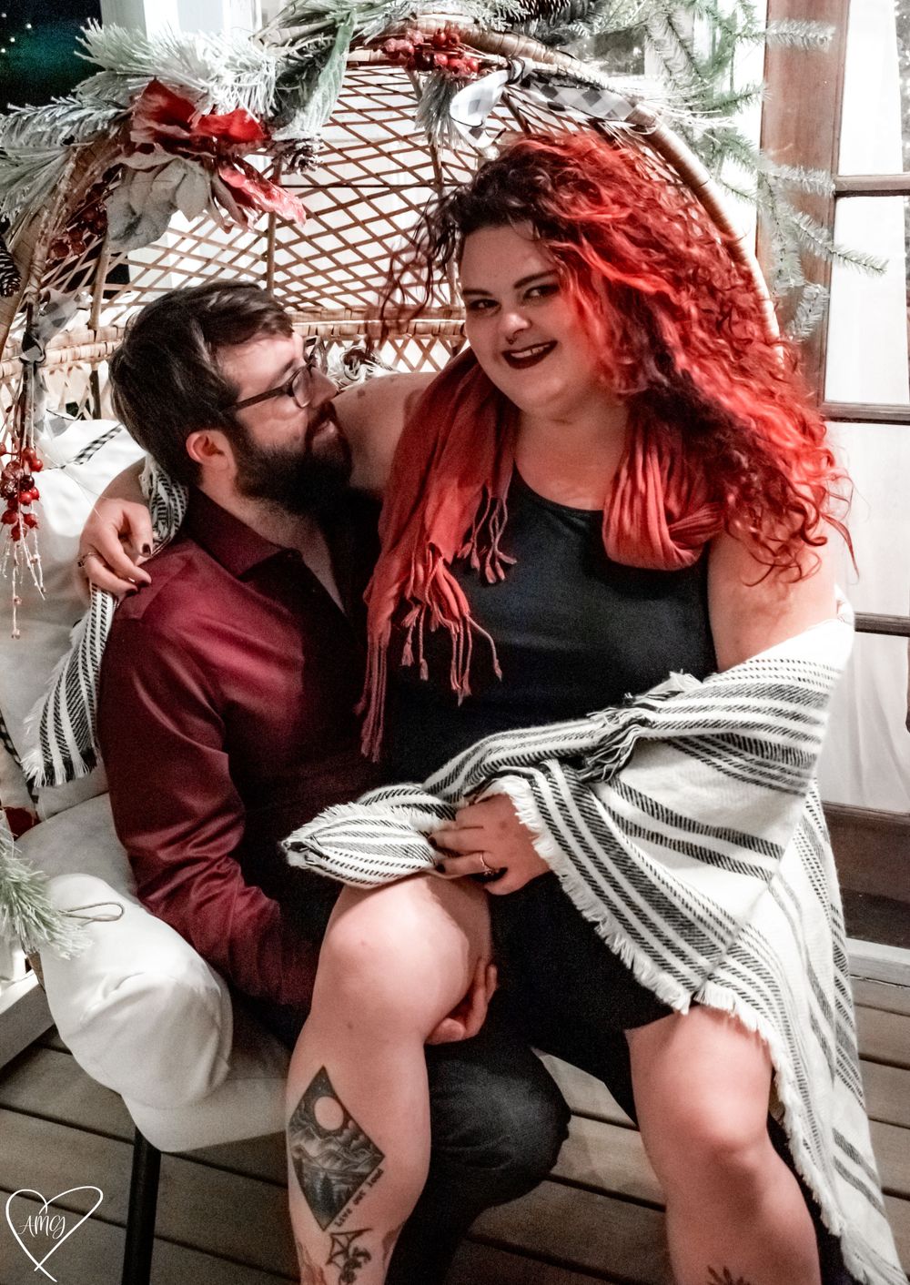 A couple together in an egg chair decorated with Christmas greenery, the woman with red hair sitting on the man's lap. Couples Photographer.