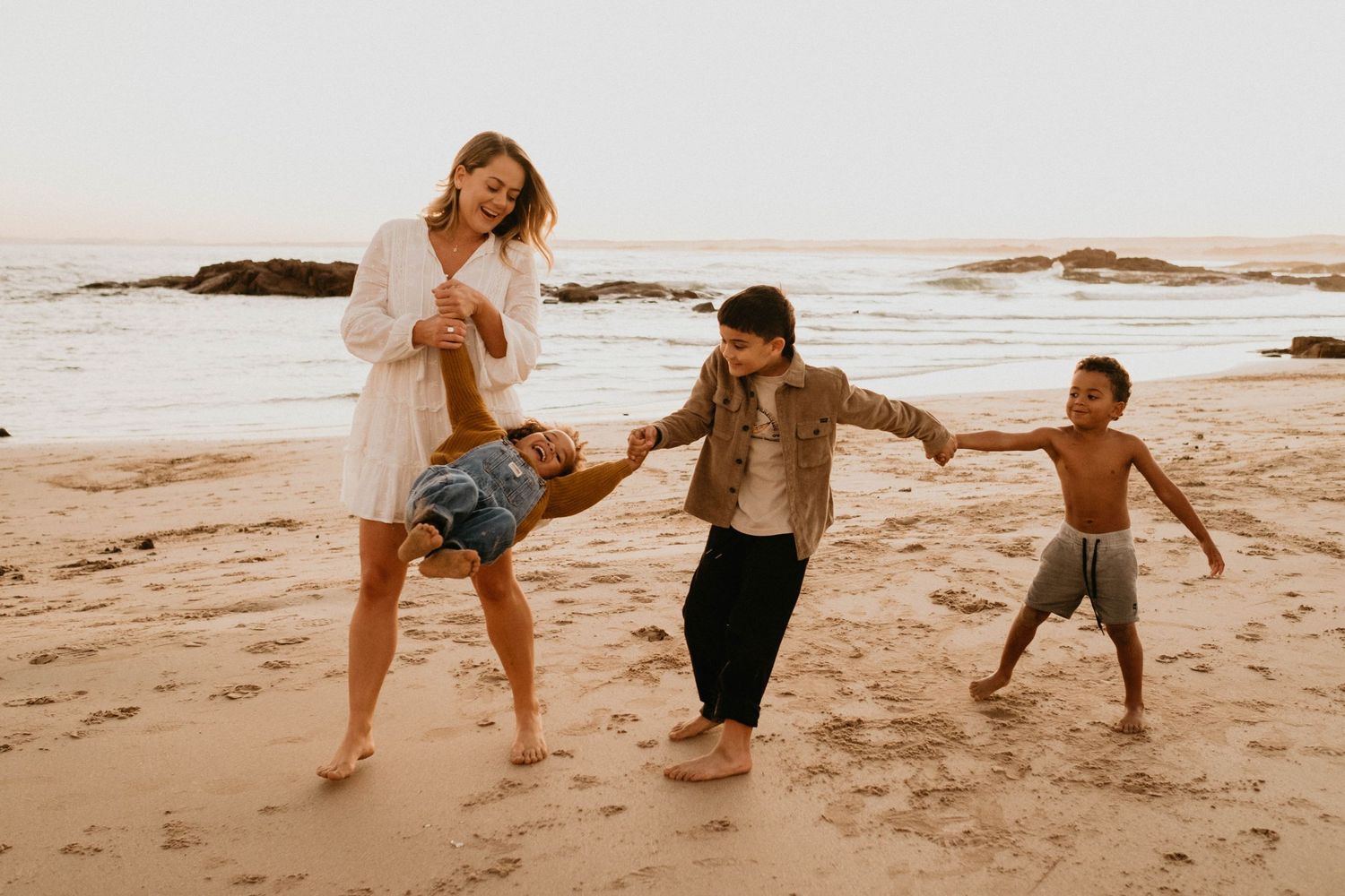 Family playing and running together on a sandy beach at sunset.