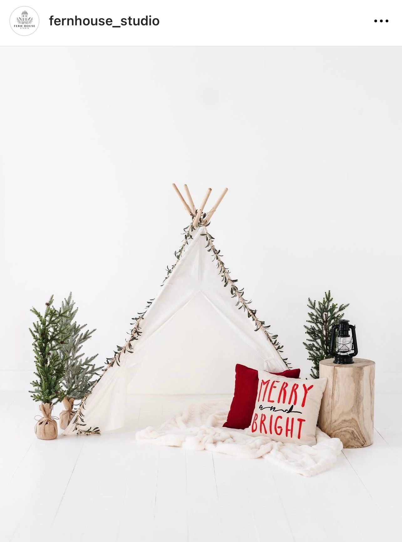 White teepee tent decorated with fairy lights and holiday pillows in a minimalist Christmas setting.