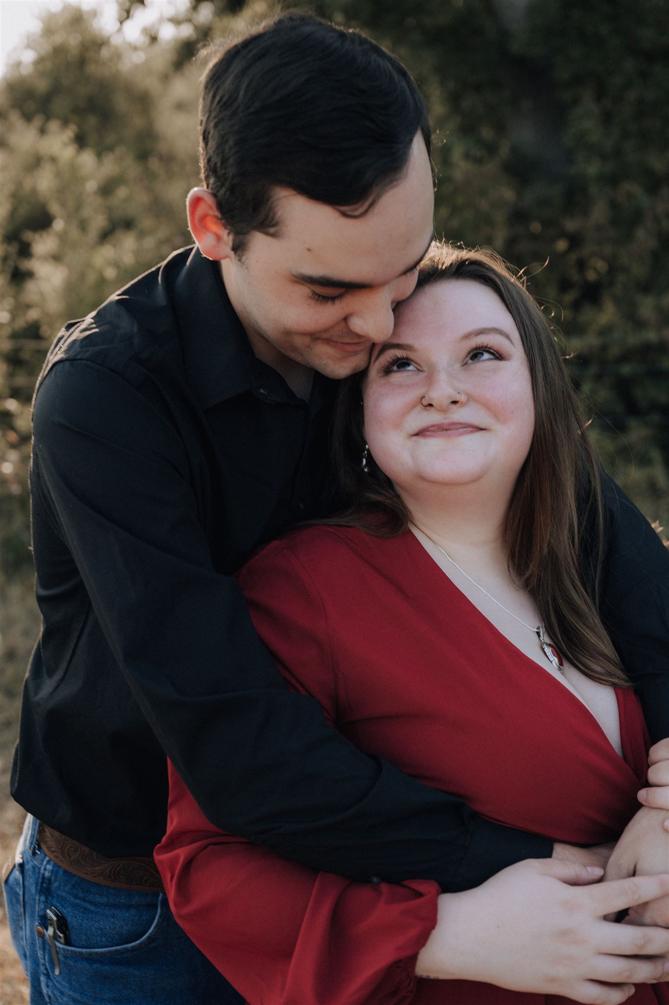 A tender moment between a couple in black and red outfits during an outdoor photoshoot.