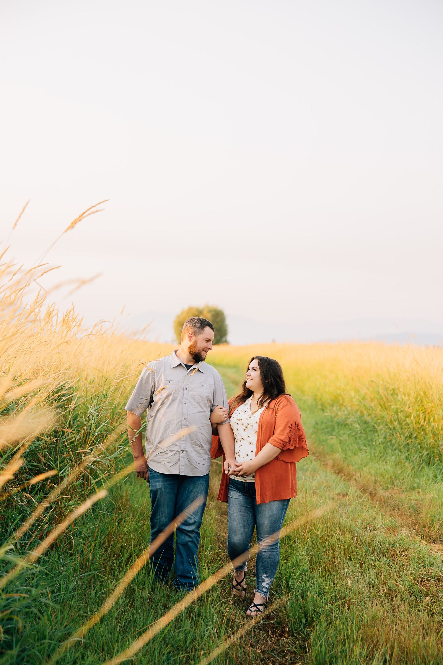 A couple walking together through tall golden grass in a romantic countryside setting at sunset.