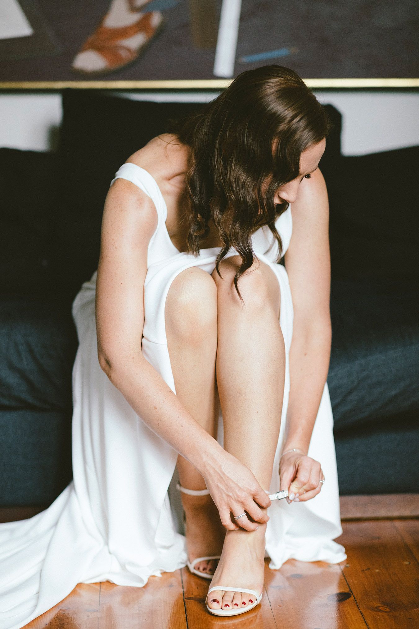 Someone in a white dress adjusting strappy sandals while seated.