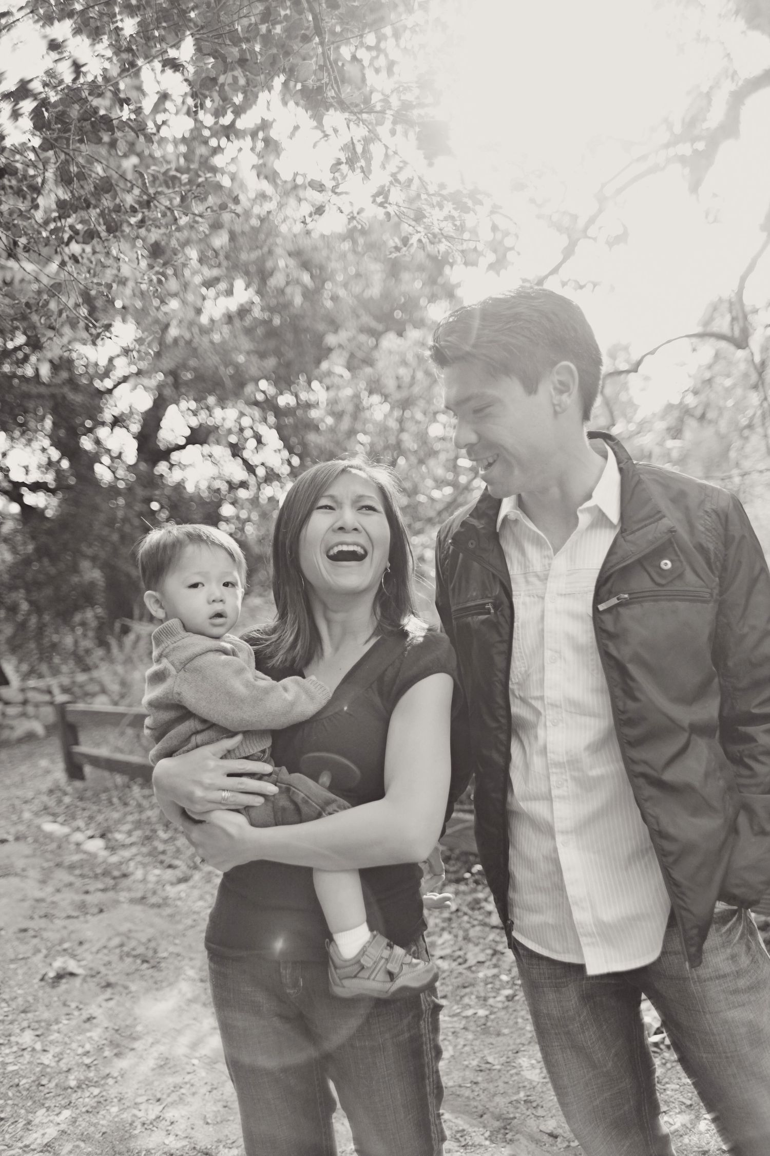 Family enjoying a candid outdoor moment together with their young child in a black and white portrait.