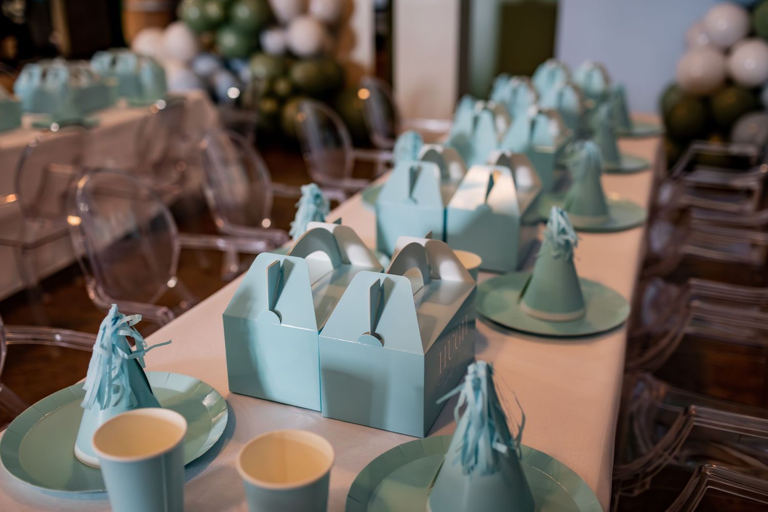 Close-up of mint green party favor boxes and teacups arranged on wooden tables.